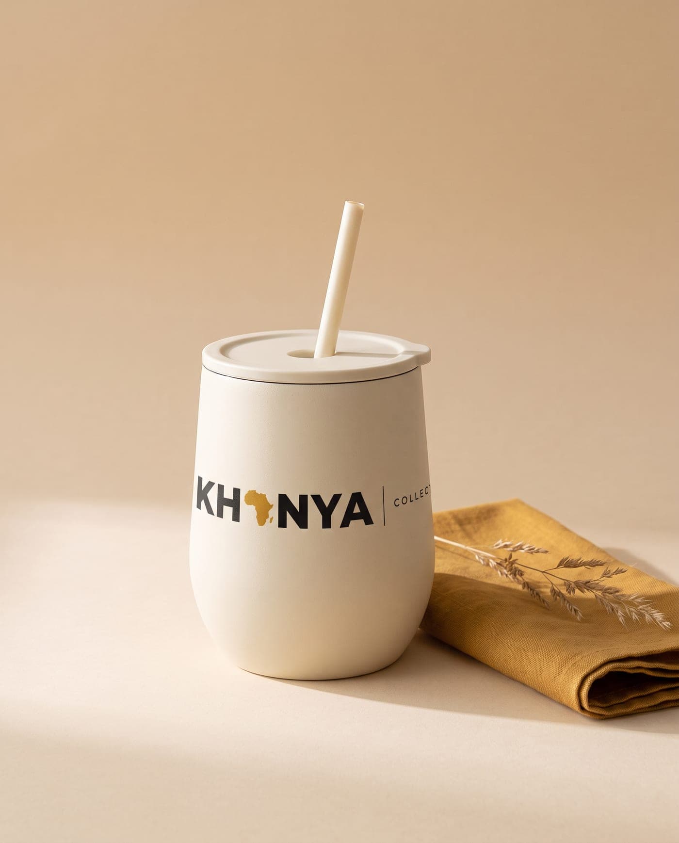 Cream tumbler with a printed Khanya Collective logo beside an ochre linen napkin