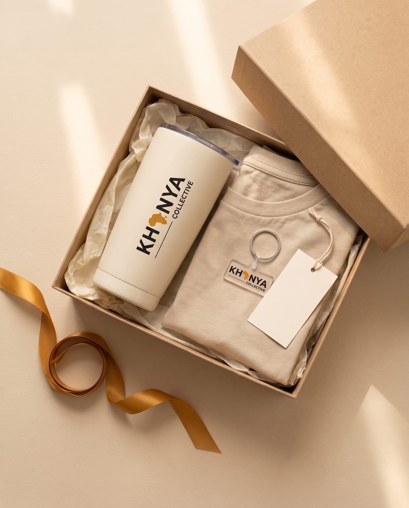 Open kraft gift box with a branded tumbler, keyring, folded T-shirt and gift tag